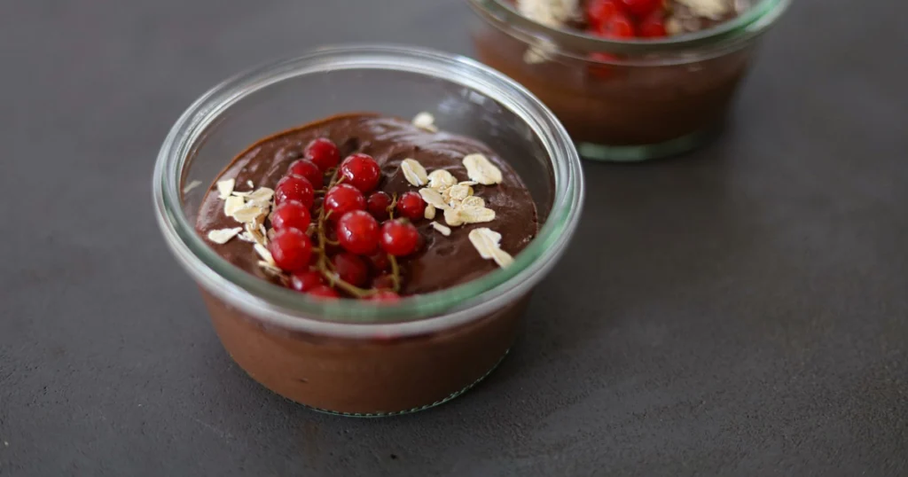 A creamy bowl of chocolate cottage cheese pudding garnished with dark chocolate shavings and fresh berries, served in a clear glass bowl on a wooden table.